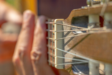 A man sits in the courtyard of a village house and plays an acoustic guitar. Close-up. Soft focus