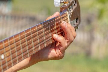A man sits in the courtyard of a village house and plays an acoustic guitar. Close-up. Soft focus