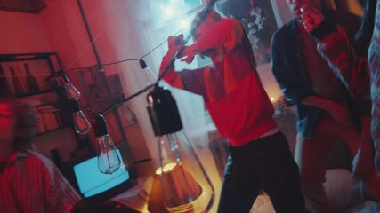Group of young multiethnic men and women dancing together in vintage room decorated with garland at home party while friend filming them with retro camcorder