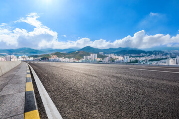 Asphalt road and modern city skyline with mountain landscape.