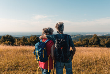 Active senior couple hiking in nature with backpacks, enjoying their adventure at sunset.