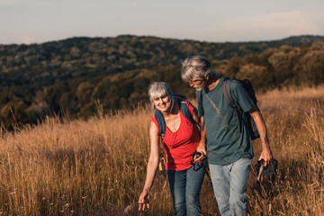Active senior couple hiking in nature with backpacks, enjoying their adventure at sunset.