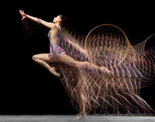 Portrait of young girl rhythmic gymnast in motion and action isolated in mixed light on dark...