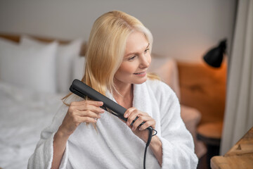 Blonde pretty woman making hairstyling by using a flat iron
