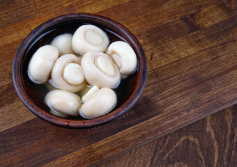 A plate with pickled champignons on a wooden board.