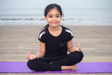 Cute little girl meditating on exercise mat at beach