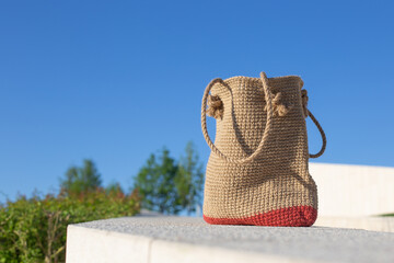 Brown knitted bag on concrete podium in front of blue sky in the park. Eco-friendly shopping jute...