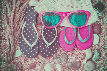 Beach scene. Sun straw hat, two pairs of flip flop sandals, and sunglasses lying on sea coquina...