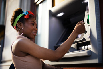 Beautiful african womn using ATM machine. Attractive young woman withdrawing money from credit card...