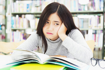 The tired schoolgirl lies with her head on the table and looks at a pile of textbooks . Education Concept