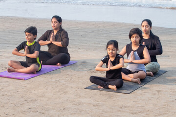 Two women with boys and little girl meditating in prayer pose sitting at the beach