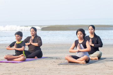 Two women with boys meditating in prayer pose sitting at the beach