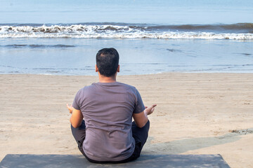 Rear view of man meditating in yoga lotus position at seafront