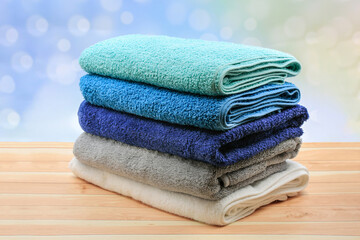 Stack of colorful towels on wooden table over bokeh background.