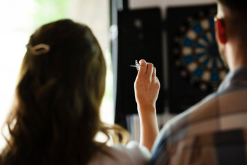 Young colleagues taking break after work. Happy young businessman and businesswoman playing darts...