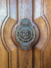 Door handle like antique head on the entrance of a house on Malta. Italian traditional doorknob. Old ornate metal decoration on wooden background.