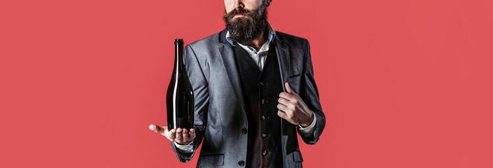 The person holds a red wine bottle in a hand. Man holding bottle with champagne, wine. Bearded man with a bottle champagne of and glass
