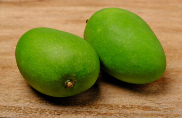Two fresh green raw mangoes on wooden background