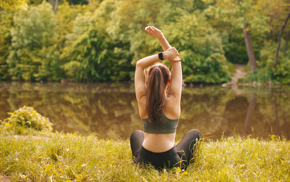 Photo of young sport woman making stretching outdoor on grass near lake during sunrise