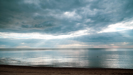 Fototapeta na wymiar Calm sea on a summer evening with cloudy skies and sunbeams breaking through the clouds.