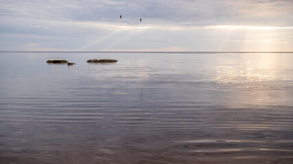 Fototapeta premium Calm sea on a summer evening with cloudy skies and sunbeams breaking through the clouds.
