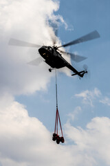 Flying helicopter carrying small vehicle with cloudy blue sky as background. © jack-sooksan