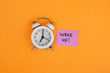 White vintage alarm clock and a sticker with an inscription Wake Up on an orange background.