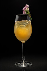 Close up glass of orange cocktail decorated with a flower on black background.