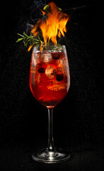 Forest aperol spiritz cocktail with fire from lime on black background.