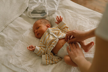 Happy young mother playing with baby while changing his diaper on bed. - Powered by Adobe