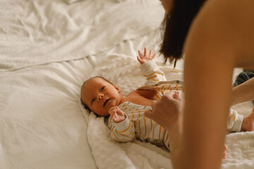 Happy young mother playing with baby while changing his diaper on bed.