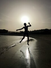 Child, boy silouette jumps at the beach with sun as halo nearly at sunset, trees in the shadows in...