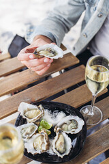 A plate of oysters, two glasses of white wine on a wooden table in a bar. Man holding an oyster 