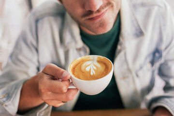 Close up picture of a man holding a cup of flat white coffee and smiling