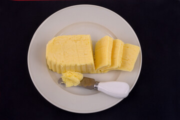 Beurre dans une assiette avec un couteau vu de dessus sur fond noir