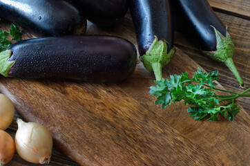 Whole raw eggplant, onions and parsley on wooden cutting board.