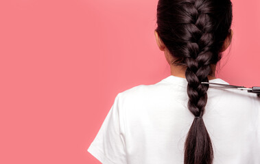 Back view of Asian woman with braided hairstyle is cutting with scissors for donate to cancer patients. Hair donation for breast cancer person. Woman with black long har braid on pink background. - obrazy, fototapety, plakaty