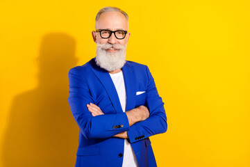 Photo portrait of senior man in blue suit glasses smiling with crossed hands isolated bright yellow color background