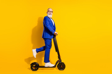 Full length body size profile side view of nice cheerful chic man riding scooter having fun isolated over bright yellow color background © deagreez