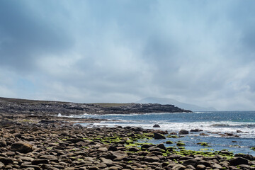 Seascape view on rough stone coast line with stones covered with green moss. Clear blue sky, Achill...