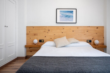 Bright white bedroom interior decorated with a photo of sea waves and a wooden headboard