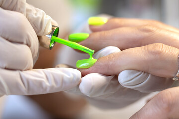 Manicure in the salon, covering the nails with colored gel polish by a manicure master. The concept of professional nail care. Close-up with a copy of the space