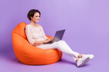 Full length profile photo of charming cheerful lady sit big soft chair use laptop isolated on...
