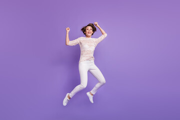 Fototapeta na wymiar Full length photo of funny lucky young woman wear knitted shirt jumping high rising fists isolated violet color background