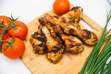 Fried chicken legs lie on a wooden board. Chicken shish kebab with a side dish of vegetables and green onions.