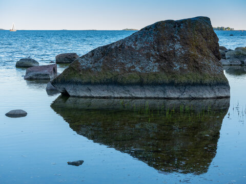 Natural rock formation on the waterfront. A large block of granite casting reflection on the water.