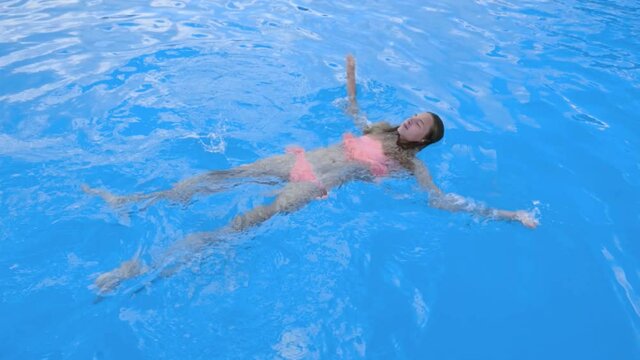 Young girl in rose bikini swims in swimming pool. Teen girl enjoys vacation in water of outdoor pool.