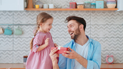 Cute little girl giving a gift to dad for a holiday in the living room. One parent with a child at home - 437026089