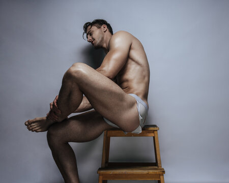 Muscular male model sitting and holding his leg in rugged white underwear