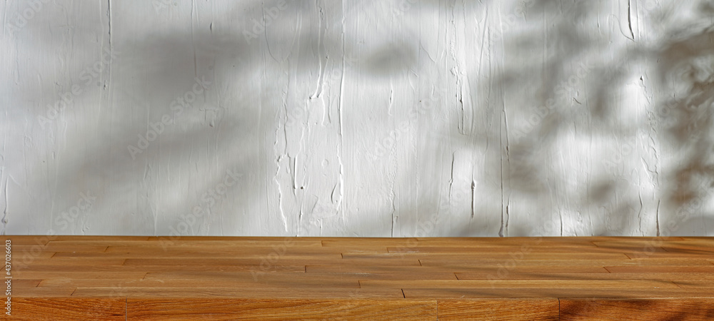 Wall mural Wooden table in the kitchen and rustic white wall with natural shade of trees and leaves, light shining through the window 